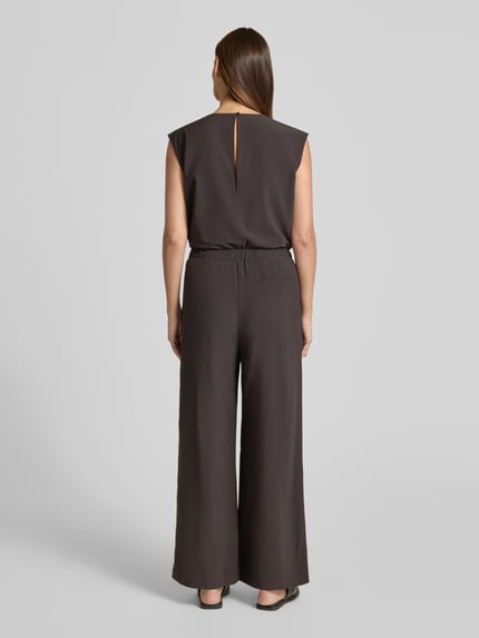 Frauenmodel trägt Relaxed Fit Jumpsuit mit V-Ausschnitt Modell 'Charlou' von Someday, Elastischer-Material-Mix, Ärmelloses-Design, Tailliert, Eingrifftaschen, Farbe Dunkelbraun, glatte Textur, Ganzkörperansicht Rückansicht. Kontext: Rückenlänge bei Größe 36: 44 cm, Brustweite bei Größe 36: 52 cm, Gesamtlänge bei Größe 36: 146 cm, Innenbeinlänge bei Größe 36: 71 cm.