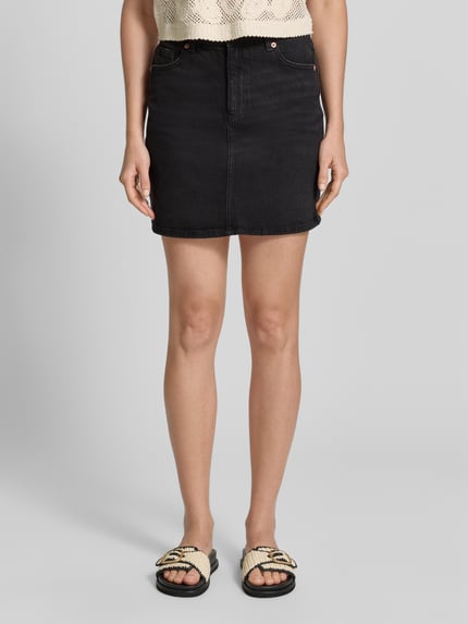 Vrouwenmodel draagt Regular Fit Jeansrok uit katoenmix model 'TESSA' van Vero Moda in zwarte denim met 5-pocket-design, label patch, riemlussen en knoop met blinde ritssluiting, twill textuur, mini lengte, vooraanzicht volledige lichaamsopname.