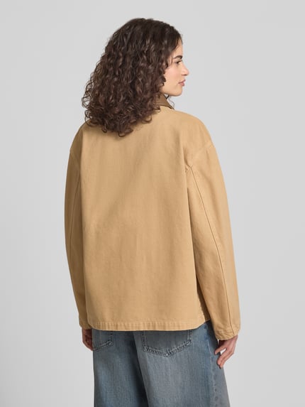Vrouwenmodel draagt Regular Fit Jeansjacke aus reiner Baumwolle Modell 'FLIMANE-1-D_B' van Hugo Blue in effen beige denim, lange mouwen, borstzak, knoopsluiting, rugaanzicht.