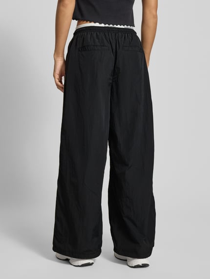 Frauenmodel trägt Regular Fit Trackpants mit Kontraststreifen von Tommy Jeans, Optik: Unifarben, Passform: Regular Fit, Applikation: Kontraststreifen, Label-Bund, Verschluss: Tunnelzug, Bundabschluss: elastisch, doppelter Bund, seitliche Reißverschlusstaschen, Gesäßtaschen; Ganzkörperansicht Rückansicht.