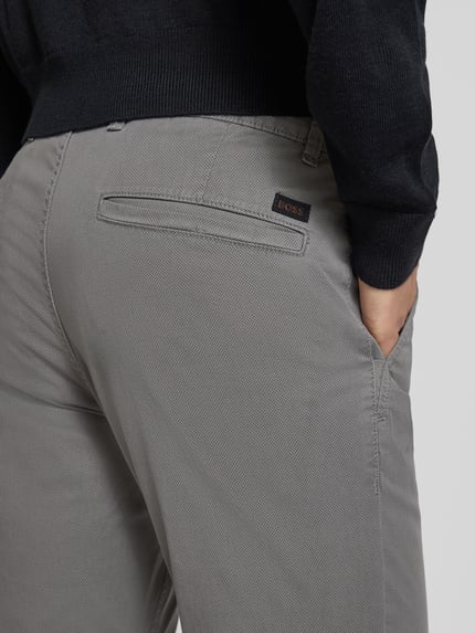 Męski model nosi Slim Fit Chino aus Baumwoll-Mix Model 'CHINO_SLIM' od BOSS, fakturowany wzór na całej powierzchni, naszywka z logo, szlufki na pasek, kieszenie z boku i z tyłu, kolor szary, mieszanka bawełny. Zbliżenie tylnej części.
