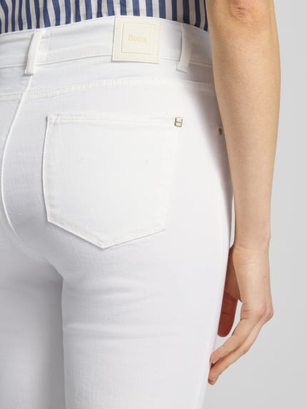 Frauenmodel trägt Bootcut Jeans mit Fransen Modell 'SHAKIRA' von Brax aus weißem Baumwoll-Mix mit Stretch, Nahaufnahme Rückansicht.