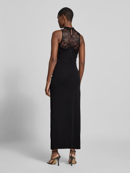 Frauenmodel trägt Maxikleid mit Spitzenrückenausschnitt von VERO MODA in Schwarz, reines Polyester, unifarben, Rückenausschnitt aus Spitze, Gehschlitz, Ganzkörperansicht Rückansicht.