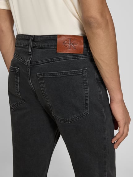 Männermodel trägt Slim Fit Jeans aus katoenmix von Calvin Klein Jeans in zwart met leren label, detailopname achterkant.
