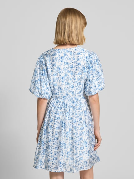 Frauenmodel trägt tailliertes Freizeitkleid aus Viskose-Mix Modell 'BLISS' von Vero Moda mit Optik:Allover-Muster, Mini-Länge, Ballonärmeln, feine Webstruktur, Ganzkörperansicht Rückansicht.