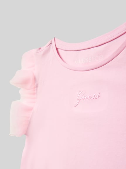 Mädchen trägt T-Shirt mit Logo-Stitching und Rundhalsausschnitt von Guess in Rosa, Tüll am Ärmel, Nahaufnahme Oberkörper.