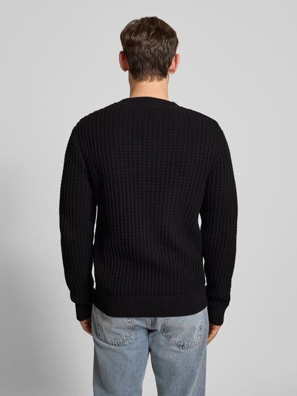 Männermodel trägt Herren Strickjacke aus reiner Baumwolle Modell 'TOM' von SELECTED HOMME, schwarz, Waffelstruktur, Grobstrick, Ganzkörperansicht Rückansicht.