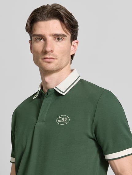 Männermodel trägt Regular Fit Poloshirt mit Logo-Print von EA7 Emporio Armani in Dunkelgrün, Kurzarm, Polokragen, Nahaufnahme Oberkörper.