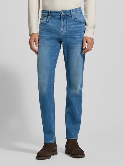 Mężczyzna nosi Jeansy z 5 kieszeniami Model 'Mitch' od JOOP! Jeans, mieszanka bawełny ze streczu, krój slim fit, zapięcie na guzik i zamek, niebieskie, logo, widok całej sylwetki z przodu.