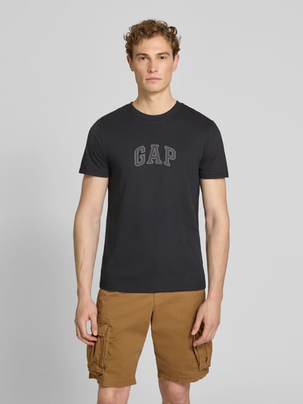 Männermodel trägt T-Shirt mit Logo-Patch und Rundhalsausschnitt von GAP aus reiner Baumwolle, Straight Fit, schwarze Farbe, Ganzkörperansicht von vorne. Rückenlänge bei Größe M: 70 cm.