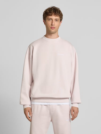 Männermodel trägt Oversized Sweatshirt mit Label-Stitching von Pegador in Hellrosa aus Baumwoll-Mix, Rundhalsausschnitt, Ganzkörperansicht von vorne.
