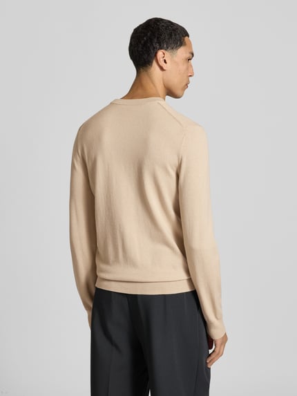 Männermodel trägt Wollpullover mit gerippten Abschlüssen von Filippa K in Beige, gerader Schnitt, Rückenlänge 68 cm, Ganzkörperansicht Rückansicht.