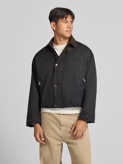 Männermodel trägt schwarze Twill Jacke mit Label- und Motiv-Stitching von ANOTHER COTTON LAB, strukturierte Oberfläche, Ganzkörperansicht von vorne.