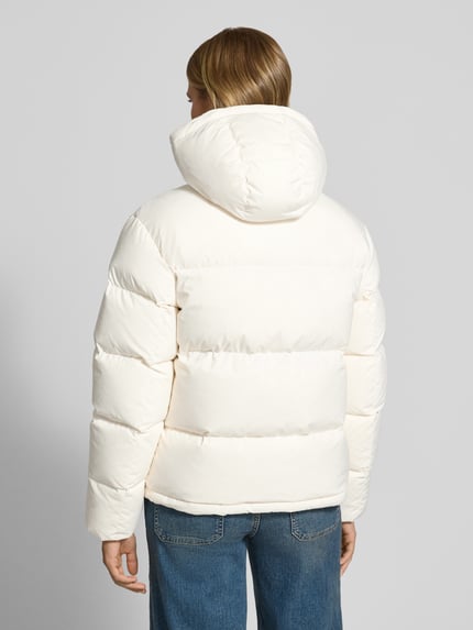 Frauenmodel trägt Regular Fit Steppjacke mit abnehmbarer Kapuze von Tommy Jeans in Weiß mit glatter Textur, Ganzkörperansicht Rückansicht. Damen Steppjacke von Tommy Jeans.