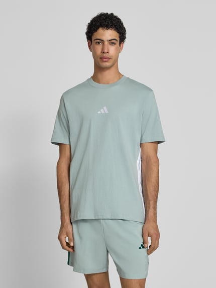 Männermodel trägt Regular Fit T-Shirt aus reiner Baumwolle von adidas Sportswear, Optik: Unifarben, Logo-Stitching, Kontraststreifen, Rundhals, Kurzarm, Ganzkörperansicht von vorne.