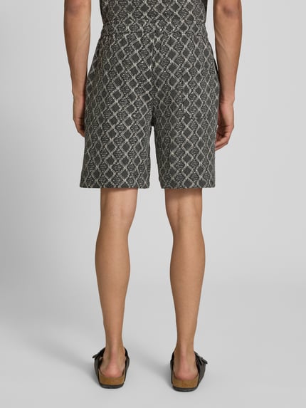 Männermodel trägt Shorts im Allover-Look mit Kordelzug Modell 'CARLOS' von Redefined Rebel aus Reine Baumwolle, Ganzkörperansicht Rückansicht. Regular-Fit, elastischer Bund, dunkles Muster, Bundweite bei Größe M: 40 cm, Innenbeinlänge: 19 cm.