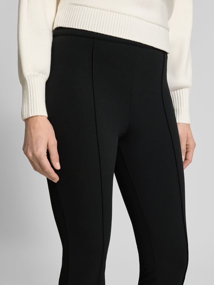 Frauenmodel trägt Flared Fit Stoffhose mit elastischem Bund Modell 'Evelina' von Guess in Schwarz, elastischer Material-Mix, Nahaufnahme Oberkörper.