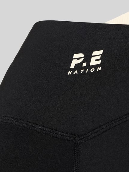 Produktfoto, High Rise Leggings in asymetrycznym kroju od P.E Nation, mieszanka materiałów z dodatkiem streczu, dopasowany krój, czarny kolor, elastyczny pas, tekstura gładka, detale szwów, logo na pasku