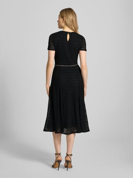 Frauenmodel trägt Midikleid mit Gürtel in Gliederketten-Optik von MICHAEL Michael Kors in Schwarz, Material-Mix mit Stretch-Anteil, taillierter Schnitt, Rundhalsausschnitt, blickdichtes Unterkleid, Schlüsselloch-Ausschnitt, Ganzkörperansicht Rückansicht.
