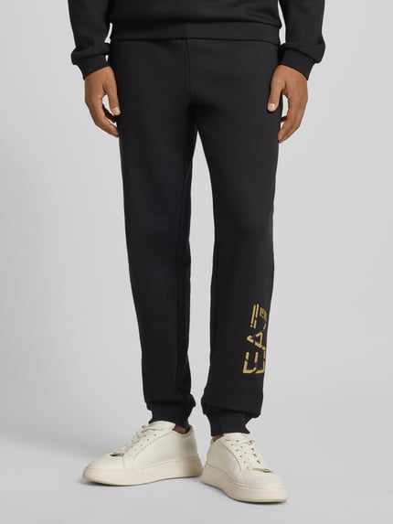 Männermodel trägt Sweatpants mit elastischem Bund und Label-Print von EA7 Emporio Armani aus reiner Baumwolle, Regular-Fit, Nahaufnahme Unterkörper.