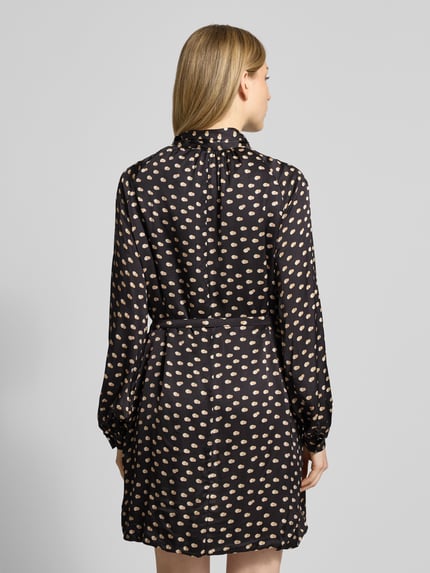 Frauenmodel trägt Cocktailkleid mit Stehkragen von Rinascimento aus reiner Viskose mit Schleifen-Detail und Taillengürtel, Ganzkörperansicht Rückansicht.