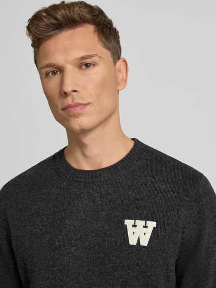 Männermodel trägt Strickpullover aus Lammwolle Modell 'Tay' von Wood Wood, Regular-Fit, Rundhalsausschnitt, Label-Stitching, Nahaufnahme Oberkörper.