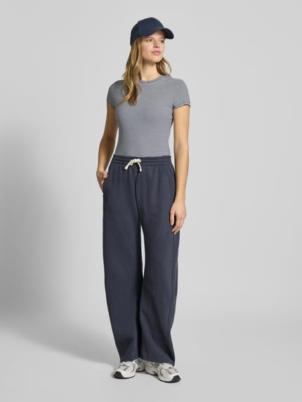 Kobiece modelka nosi Slim Fit T-Shirt mit Rundhalsausschnitt von REVIEW, elastyczna mieszanka bawełny, krój slim fit, okrągły dekolt, krótki rękaw, długość tyłu w rozmiarze S: 52 cm, widok całej sylwetki z przodu.