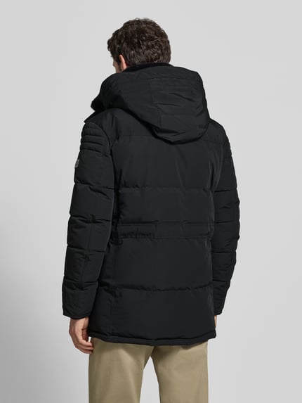 Mannenmodel draagt Parka mit Kapuze von NAUTGÅRD 'J-LHOTSE 226', zwart, longline met labeldetail, kap, zakken, tunnelkoord, Ganzkörperansicht Rückansicht.