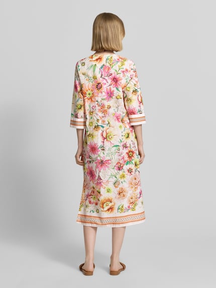 Vrouwenmodel draagt Tunikakleid im Allover-Look met V-hals van Emily Van den Bergh, rechte fit, midi-lengte, katoen, 3/4-mouw, kleurige bloemmotieven, zichtbare zoomdetails, ruglengte 115 cm, borstwijdte 46 cm, mouwlengte 44 cm, geheel van achteren.