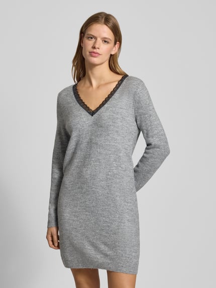 Frauenmodel trägt tailliertes, knielanges Strickkleid mit V-Ausschnitt und Spitzenbesatz, melierte Optik, Modell 'TAMMY' von Only, Nahaufnahme Oberkörper.
