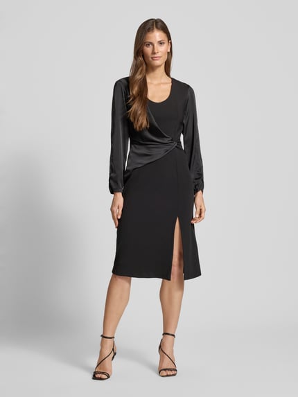Frauenmodel trägt Cocktailkleid mit Raffungen von Rinascimento aus schwarzem Material-Mix mit Stretch-Anteil, taillierter Schnitt, Wickel-Optik, U-Ausschnitt, Gehschlitz, Nahtreißverschluss, Ganzkörperansicht von vorne.