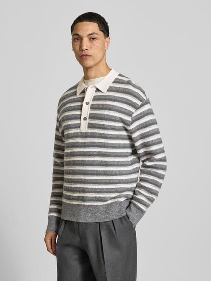 Männermodel trägt Poloshirt mit kurzer Knopfleiste von Officine Générale aus gestreiftem Feinstrick in Grau und Creme, Ganzkörperansicht von vorne.