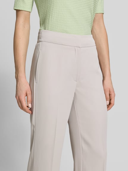 Frauenmodel trägt Stoffhose mit französischen Eingrifftaschen und Bügelfalte von Betty Barclay, hellbeige, glatte Textur, Nahaufnahme Oberkörper. Material-Mix mit Stretch-Anteil, gerader Schnitt, Haken- und Reißverschluss, Gesäßtaschen.