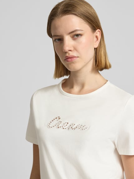 Kobiece modelka nosi damski t-shirt Regular Fit T-Shirt aus reiner Baumwolle Modell 'MIRANDA' von Vero Moda, efekt: jednolity kolor, haft angielski, okrągły dekolt, krótki rękaw, dżersej z bawełny, aplikacja, zbliżenie na górną część ciała.