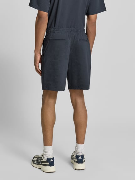 Männermodel trägt Loose Fit Shorts aus Baumwoll-Mix von Lacoste mit gestreiftem Allover-Muster, elastischem Bund und seitlichen Taschen, Ganzkörperansicht Rückansicht.