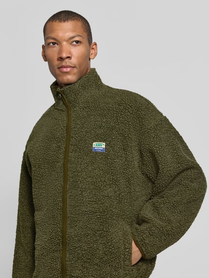 Männermodel trägt Sweatjacke Modell 'HOKTOWN' mit Logo-Patch von AMERICAN VINTAGE, unifarben, Struktur-Fleece, Stehkragen, Nahaufnahme Oberkörper.
