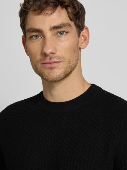 Männermodel trägt Regular Fit Strickpullover aus reiner Baumwolle Modell 'IMBERTO' von BOSS in Schwarz, Strukturmuster, Nahaufnahme Oberkörper.