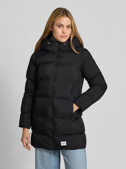 Frauenmodel trägt Regular Fit Mantel in Stepp-Optik mit Logo-Patch Modell 'TANARE' von khujo in Schwarz, Nahaufnahme Oberkörper. Damen Mantel, Zweiwege-Reißverschluss, Rückenlänge 82 cm, Schulterbreite 47 cm, Brustweite 47 cm, Ärmellänge 59 cm.