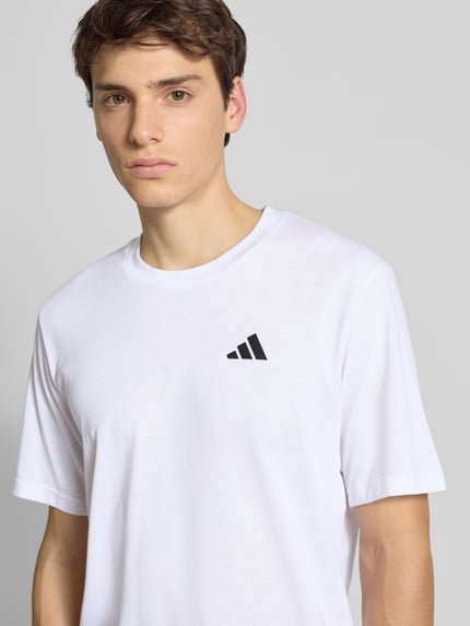 Männermodel trägt T-Shirt mit Label-Print von adidas Training in Weiß, Regular Fit, Material-Mix mit Baumwolle, Nahaufnahme Oberkörper.