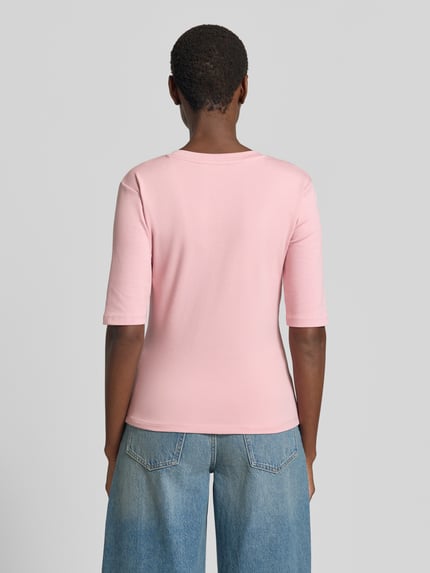 Frauenmodel trägt T-Shirt mit Rundhalsausschnitt von Christian Berg Woman aus Baumwoll-Elasthan-Mix, Slim-Fit, 1/2-Arm, Rückenlänge 53 cm, hellrosa Farbe, glatte Struktur, Ganzkörperansicht Rückansicht.