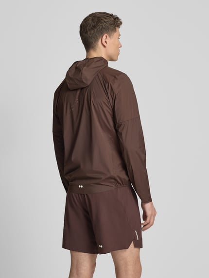 Männermodel trägt Windbreaker mit Kapuze und Logo Modell 'SENSE AERO' von Salomon, Material-Mix mit Stretch-Anteil, Regular-Fit, Rückenlänge 71 cm, Schulterbreite 44 cm, Brustweite 41 cm, Ärmellänge 67 cm, einfarbig braun, glatte Textur, Ganzkörperansicht Rückansicht.