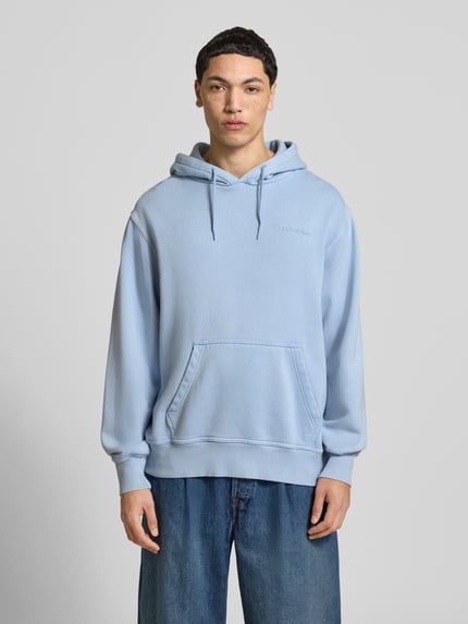 Męski model nosi Hoodie mit Label-Stitching und Känguru-Tasche od Dickies, bawełniany miks, krój relaxed fit, jasnoniebieski kolor, długość tyłu w rozmiarze M: 71 cm, długość rękawa w rozmiarze M: 65 cm, widok całej sylwetki z przodu