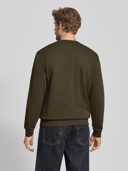 Männermodel trägt Sweatshirt mit Label-Patch von Scotch & Soda in Oliv, lockerer Schnitt, reine Baumwolle, Ganzkörperansicht Rückansicht.