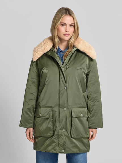 Frauenmodel trägt Daunenjacke mit Webpelzkragen Modell 'DAIMI' von BAUM & PFERDGARTEN in glänzendem Olivgrün, strukturierte Oberfläche, oversized Longline-Form mit Umlegekragen, Pattentaschen, Knöpfen und Label-Detail, Ganzkörperansicht von vorne.