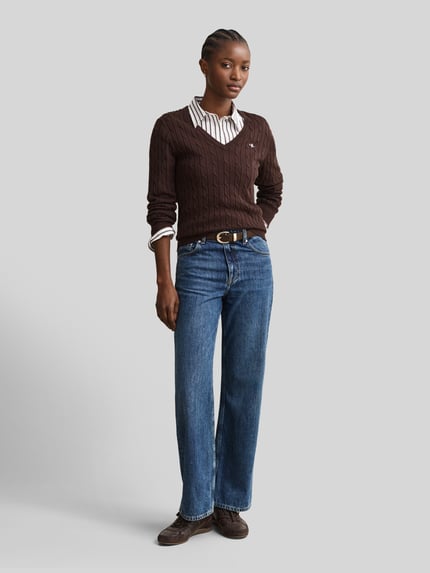 Frauenmodel trägt dunkelbraunen Regular Fit Pullover aus Baumwoll-Mix mit Logo-Stitching von GANT, blaue Jeans, Damen Pullover, Ganzkörperansicht von vorne.