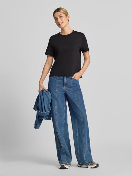 Frauenmodel trägt Regular Fit T-Shirt aus reiner Baumwolle von s.Oliver RED LABEL in Schwarz, kombiniert mit blauer Jeans, Ganzkörperansicht von vorne.