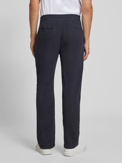 Mężczyznamodel nosi Straight Fit Sweatpants in Musselin-Optik von Lindbergh, spodnie dresowe z bawełny, ciemny granat, efekt muślinu, szerokość w rozmiarze M: 41 cm, długość wewnętrzna nogawki 81 cm, całkowity widok z tyłu.