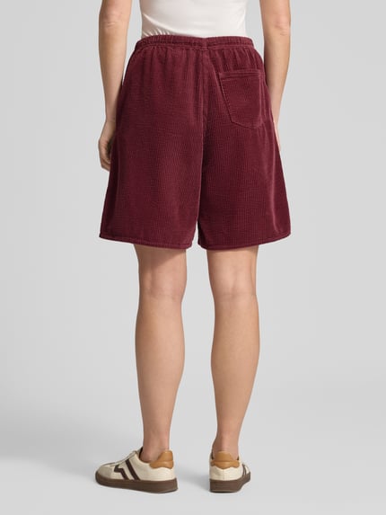 Männermodel trägt Shorts mit elastischem Bund Modell 'PADOW' von American Vintage, bordowa wiskoza, luźny krój, kieszeń z tyłu; Szerokość w rozmiarze S: 37 cm, długość nogawki wewnętrznej: 20 cm; Ganzkörperansicht Rückansicht.