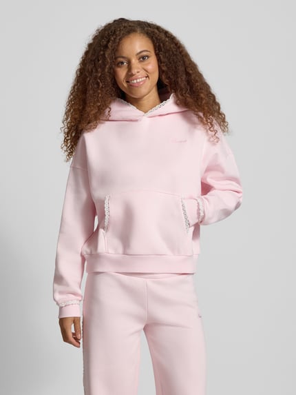 Frauenmodel trägt Hoodie mit Häkelspitzenbesatz von REVIEW in Rosa, lockere Passform, Baumwollmischung, Logo-Print, Kängurutasche, gerippte Abschlüsse, Ganzkörperansicht von vorne.