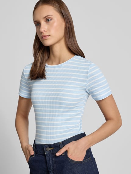 Vrouwenmodel draagt Slim Fit t-shirt uit katoenmix Model 'RUKA' van Pieces, lichtblauw-wit streepmotief, fijnrib, ronde hals, korte mouw, all-over motief, effen kleuren, materiaalverwerking: fijnrib, pasvorm: slim fit, motief: streepmotief, hals: ronde hals, mouwvorm: korte mouw, materiaal: katoenmix, fijnribstructuur, all-over streeppatroon, fijnribtextuur. Ganzlichaansvooraanzicht.